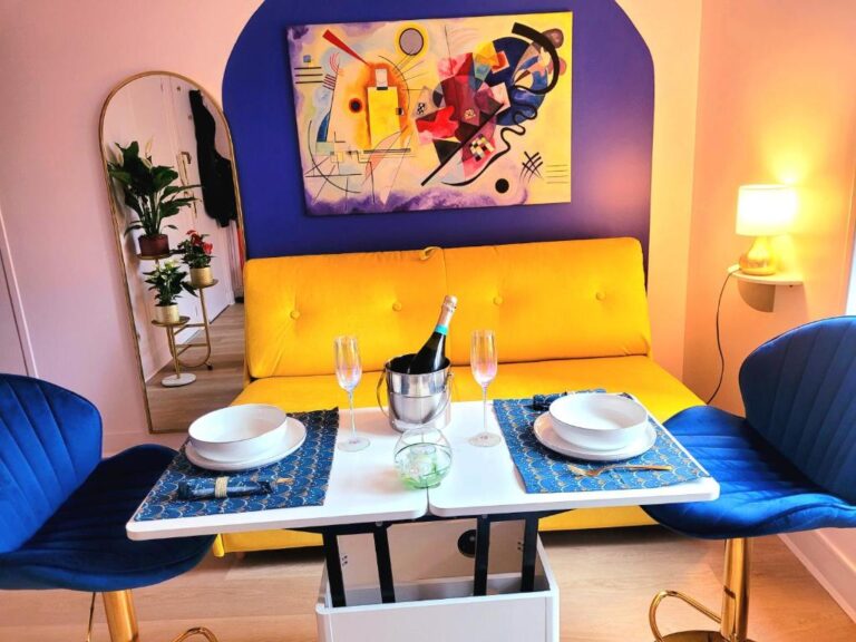 Studio chaleureux avec coin repas moderne, banquette jaune, chaises bleues et décoration artistique.